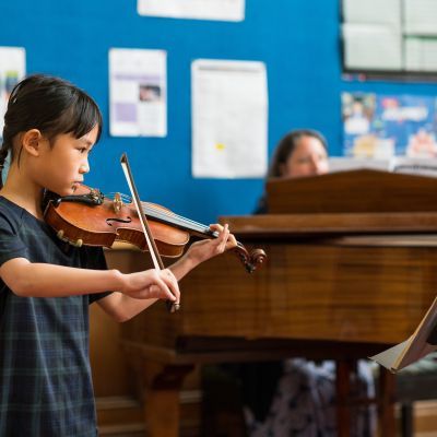 Girl in checked dress having a violin lesson with tutor on grand piano